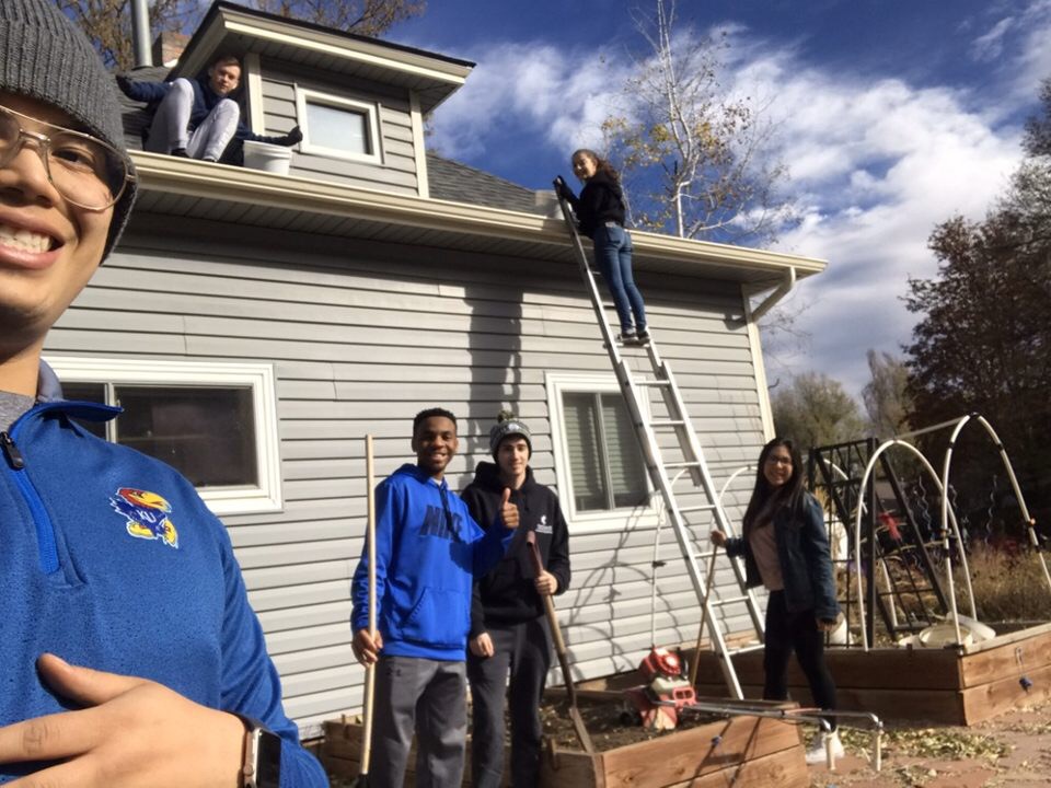A fall clean-up group standing in front of a house holding rakes